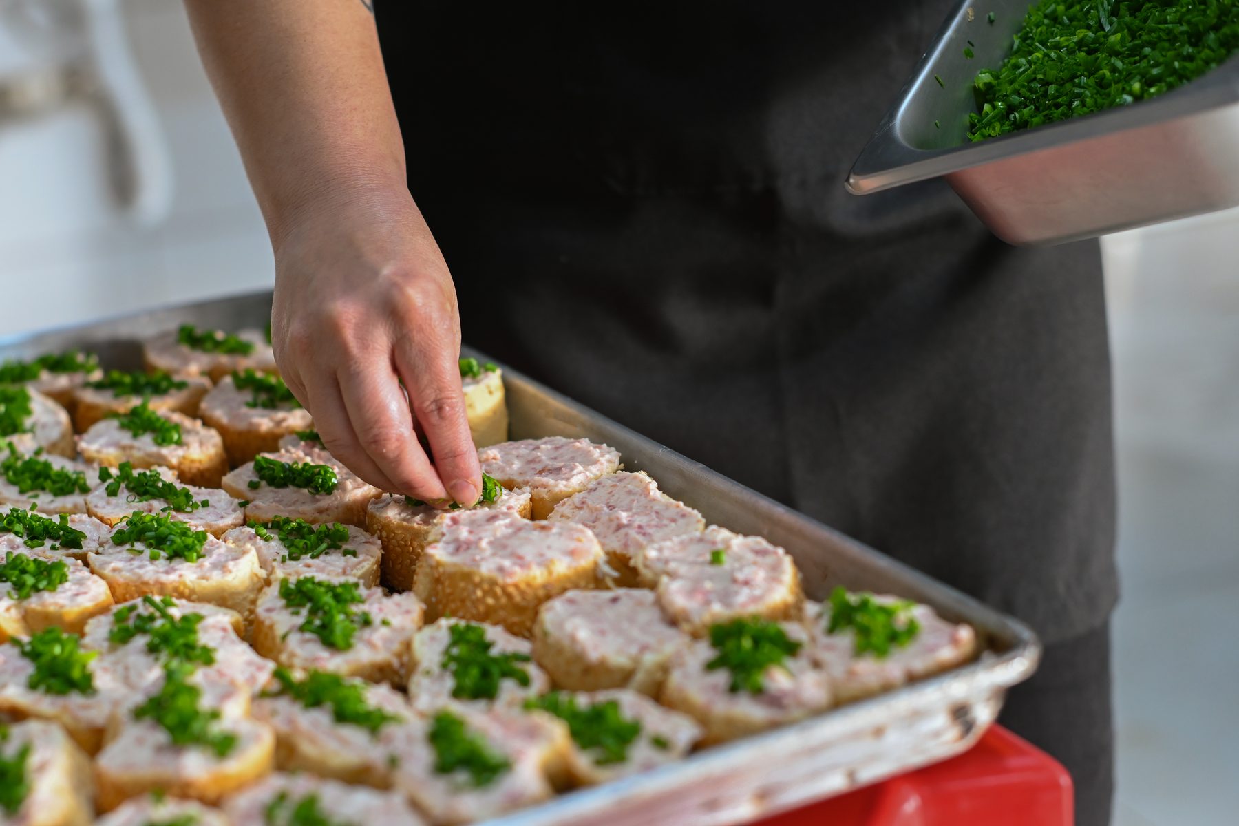 Mão da equipe finalizando canapés com cebolinha na bandeja